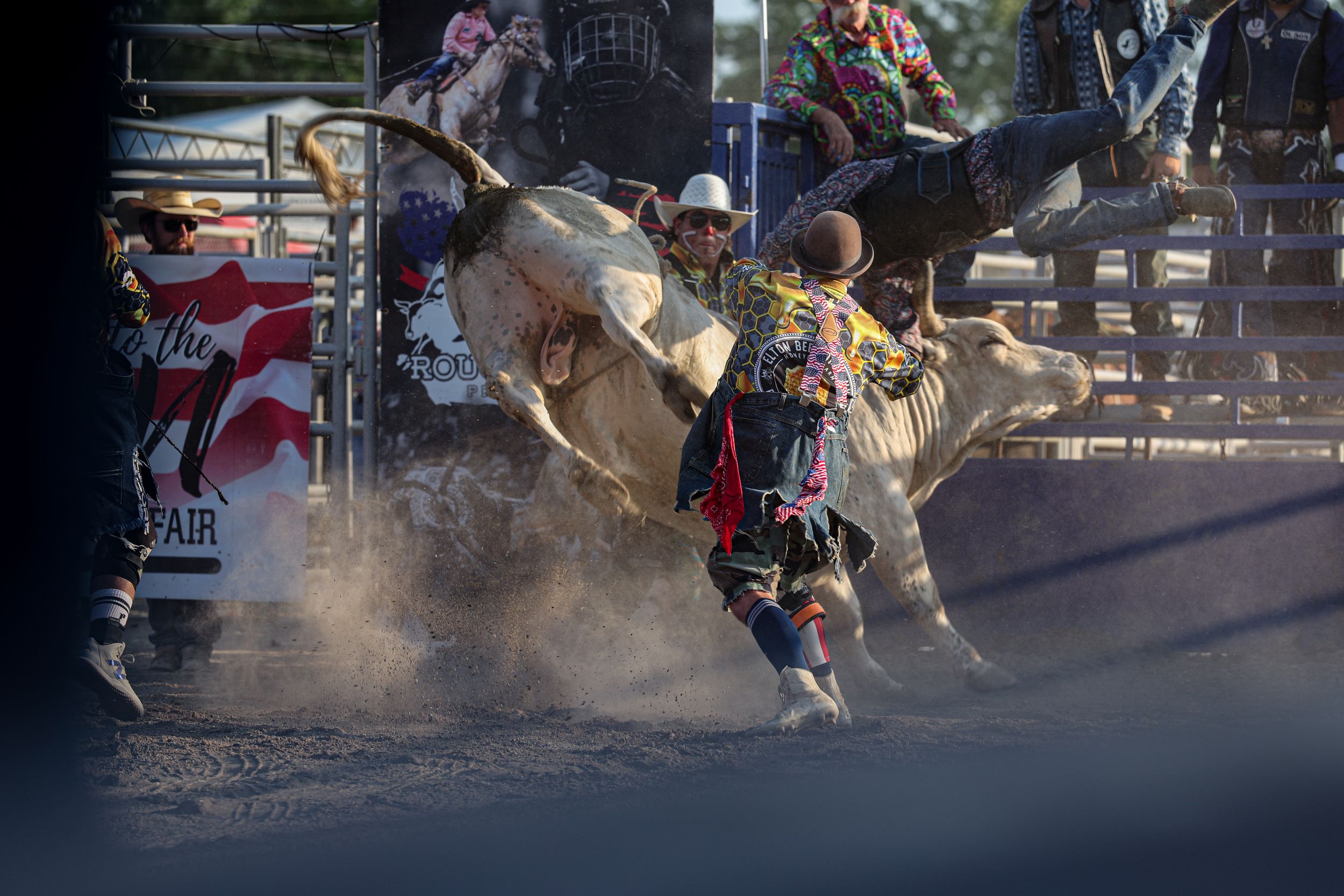 Bull rider in a cloud of dust at a backlit rodeo arena